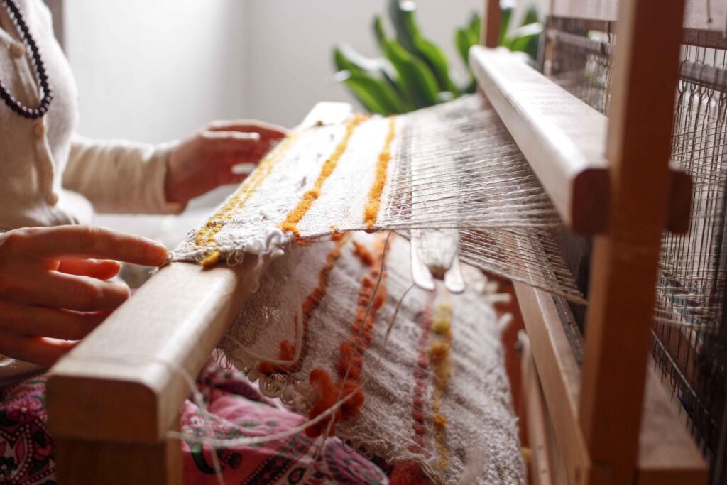 Somebody using a loom to weave orange and white yarn into a fabric