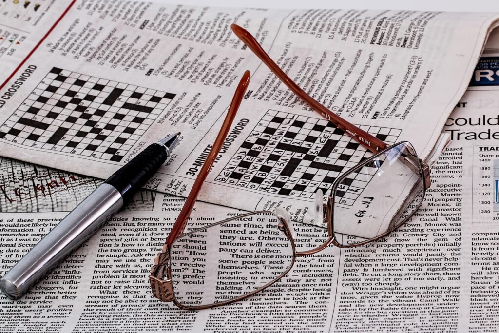 A newspaper crossword section with a pen and a pair of glasses on the newspaper