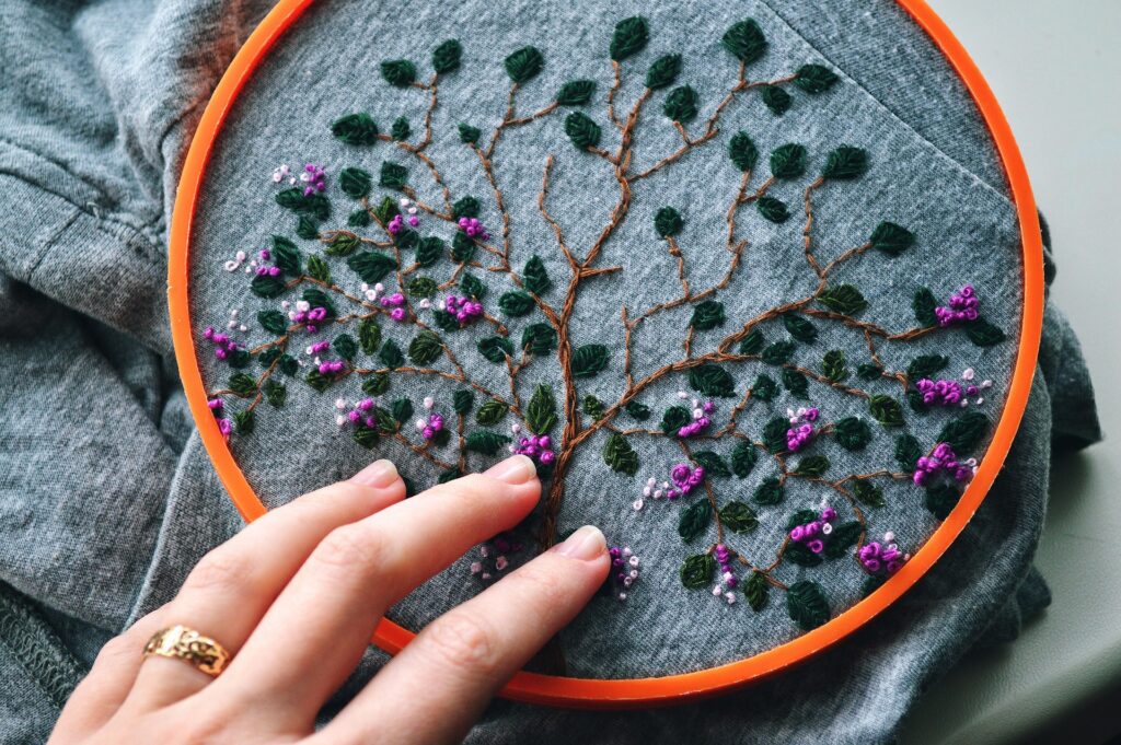 An embroidery piece featuring a tree with purple flowers being touched